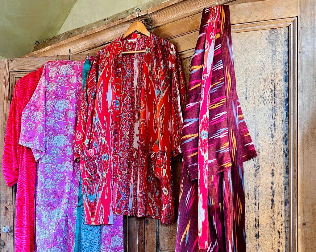 Caro London's pink and red printed kimonos in long and short lengths hanging from the top of a door