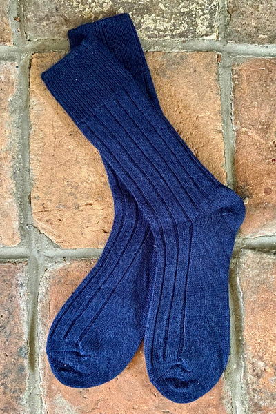 a pair of dark blue alpaca wool British made socks lying flat on tiled floor