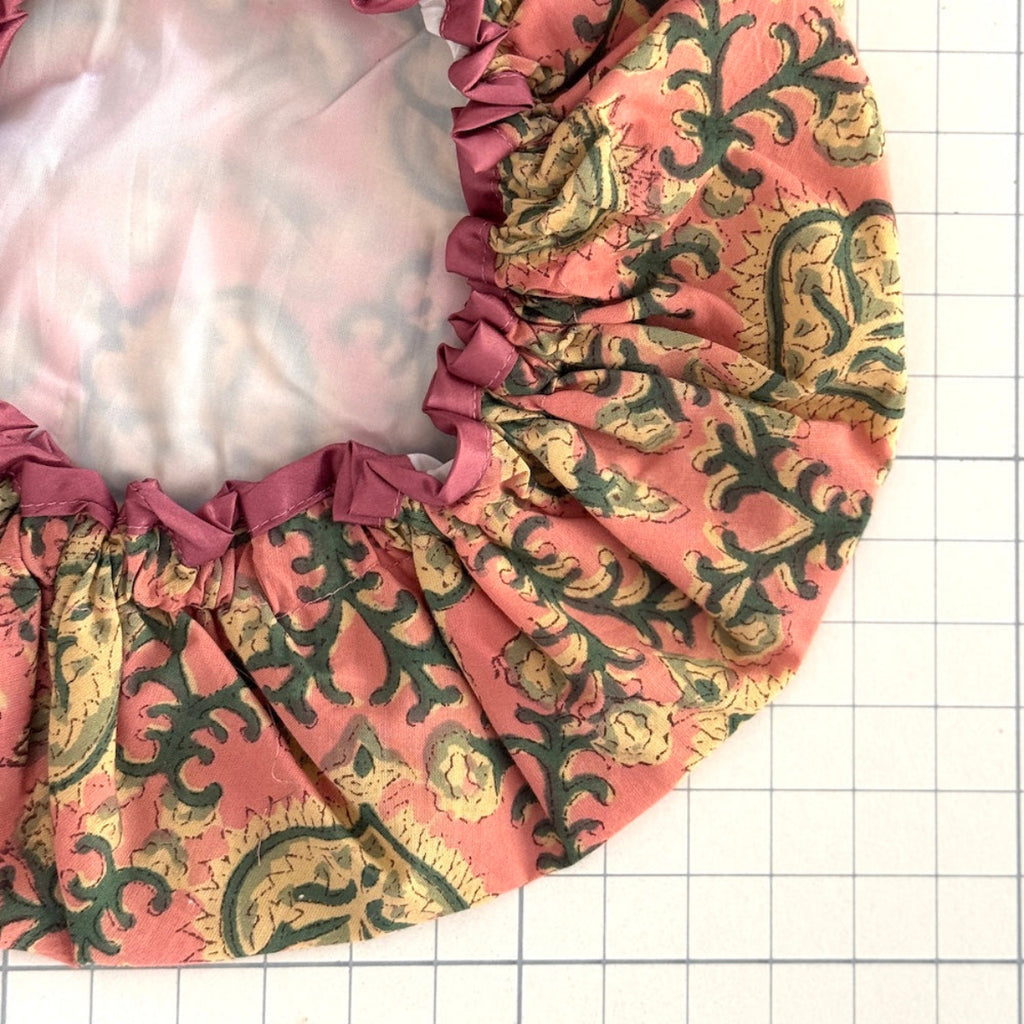 Close up of floral print bath hat in antique pink, cream and green colour palette