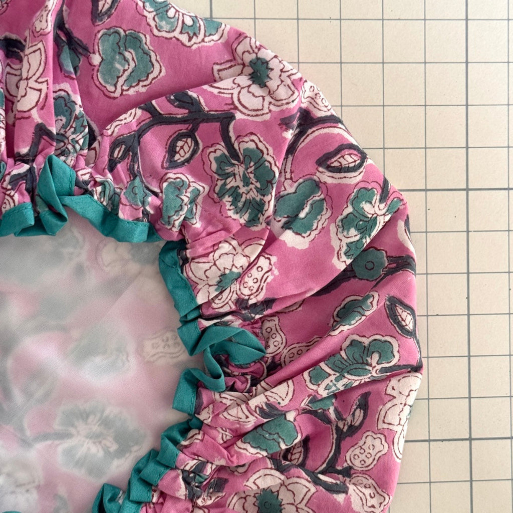 close up of pink floral print bath hat with green trim and white water resistant lining