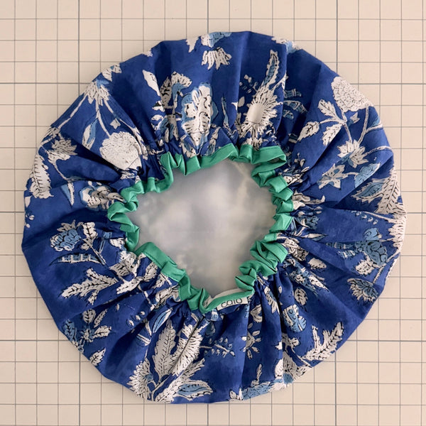 Blue and white floral print bath hat with turquoise binding on grid background