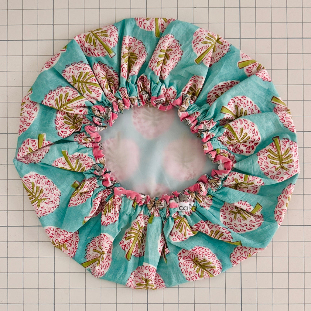 Fabric flower bath hat with pink and green floral pattern on a grid background