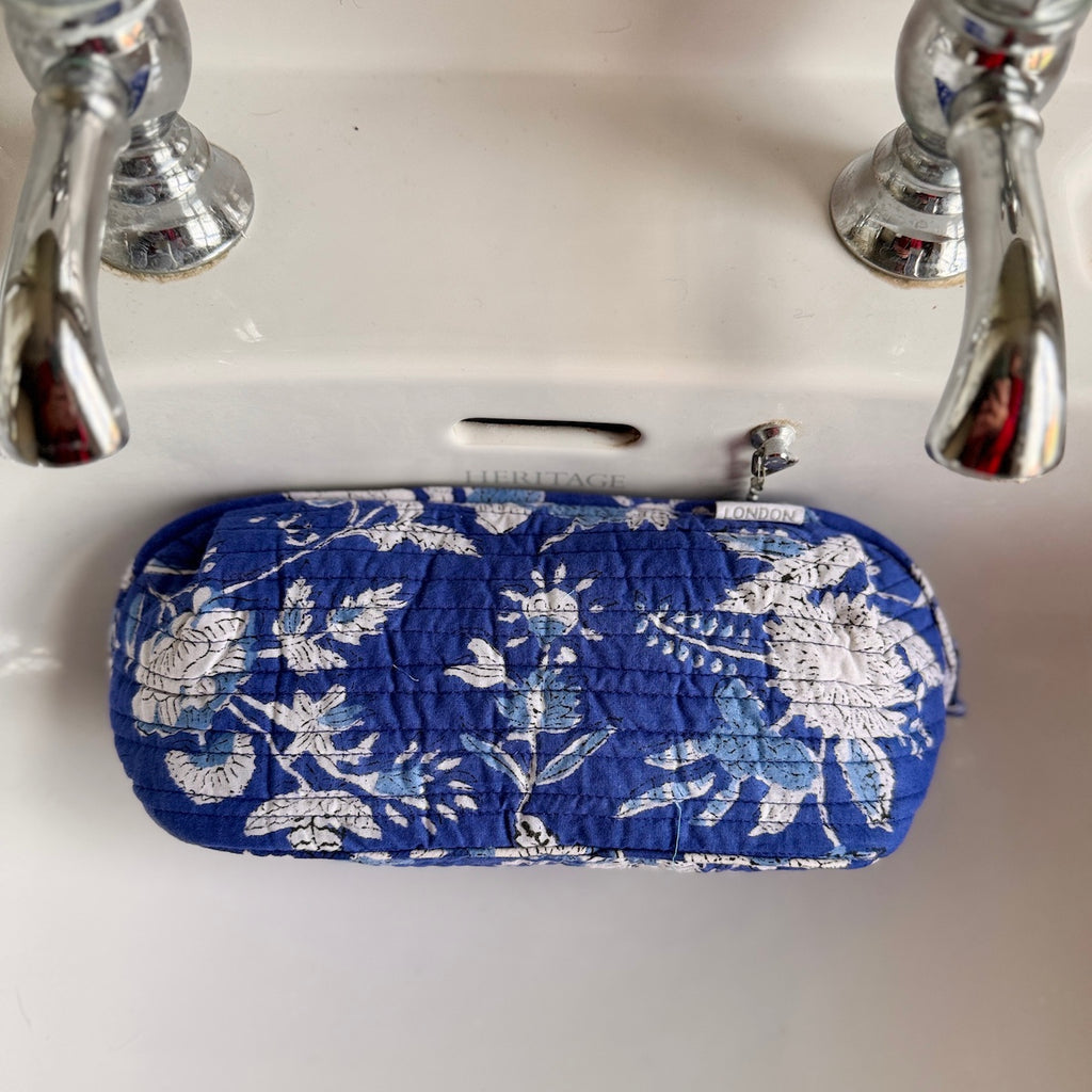 Blue floral-patterned make up bag under a faucet on a white sink