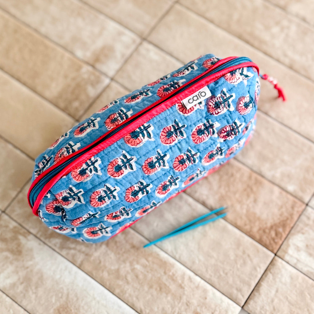 Blue quilted cosmetic bag with red flowers and zipper on beige tiles