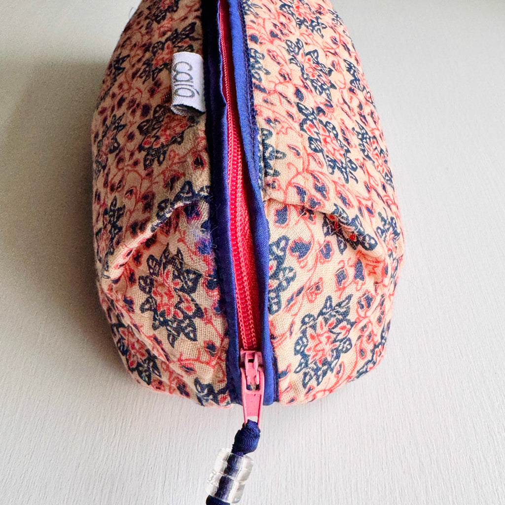 close up of long, quilted make up bag in peach and blue floral print with dark blue trim