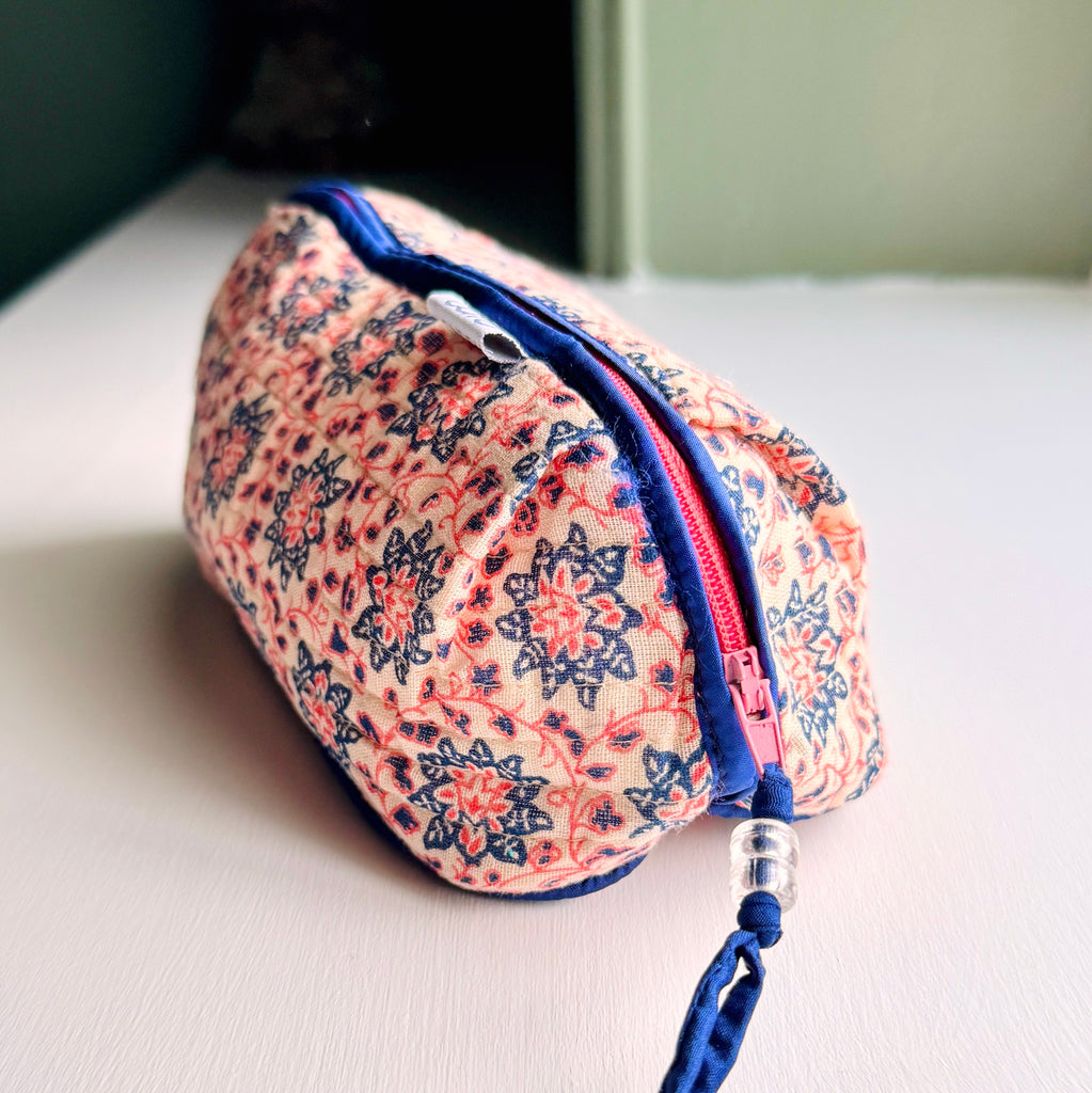 Over view of long, quilted make up bag in peach and blue floral print with dark blue trim