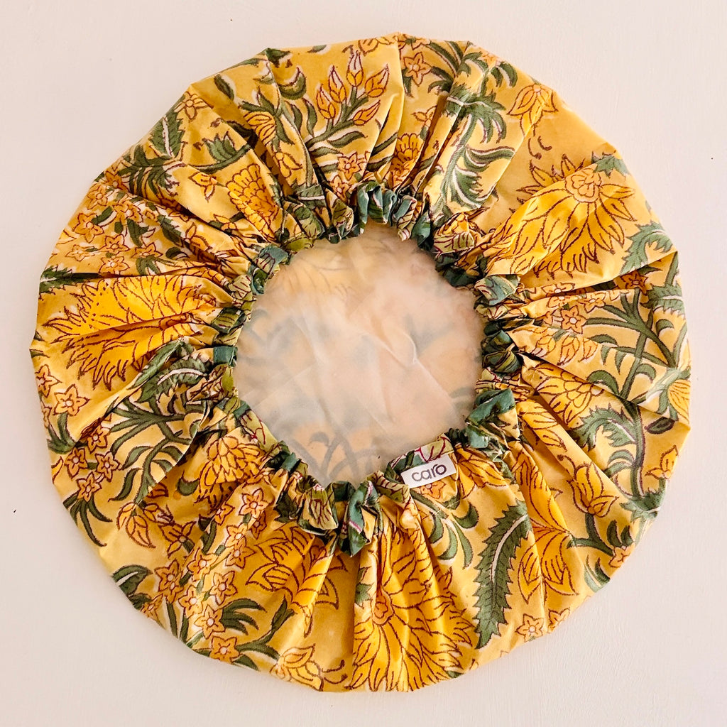 Shower Cap in vibrant yellow floral pattern with green leaves, displayed on a light-colored surface.