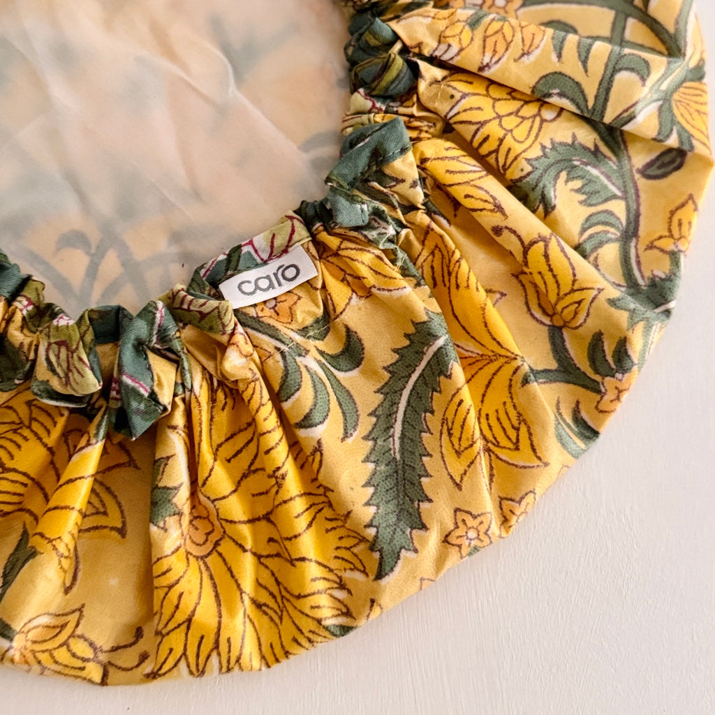 Close up of shower Cap in vibrant yellow floral pattern with green leaves.