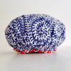 A crinkled fabric shower cap with a navy blue and white leaf pattern, finished with a red and white elastic trim, shown on a light gray background.
