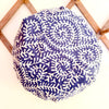 A round shower cap with a blue and white coral pattern hanging from a wooden rack on a white wall