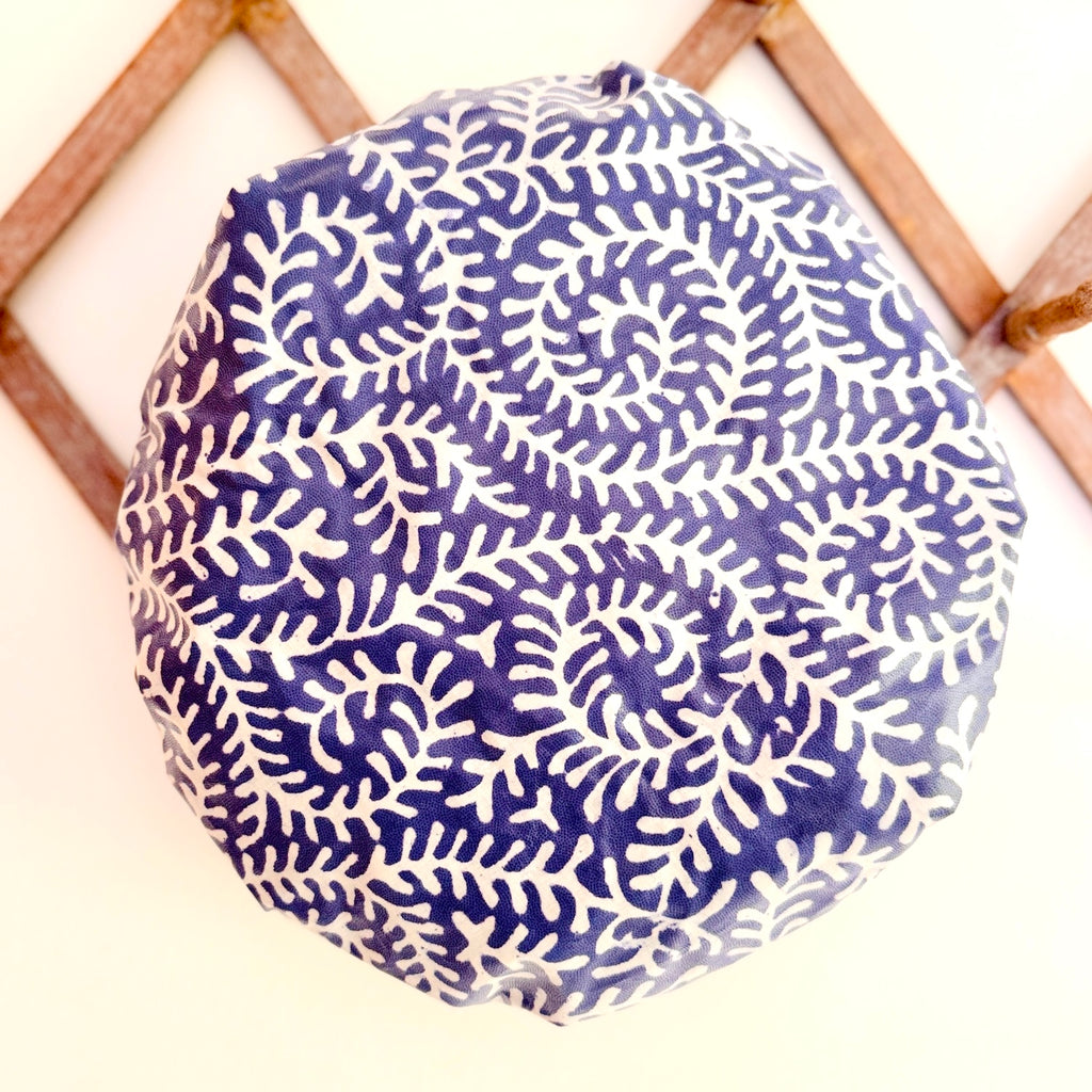 A round shower cap with a blue and white coral pattern hanging from a wooden rack on a white wall