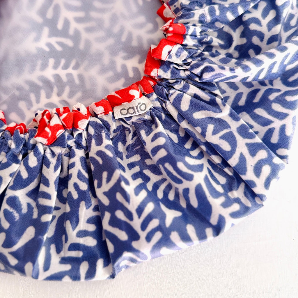 Close-up of a shower cap with a blue and white coral-like pattern, red elasticized edges, and a small visible 'caro' brand tag.