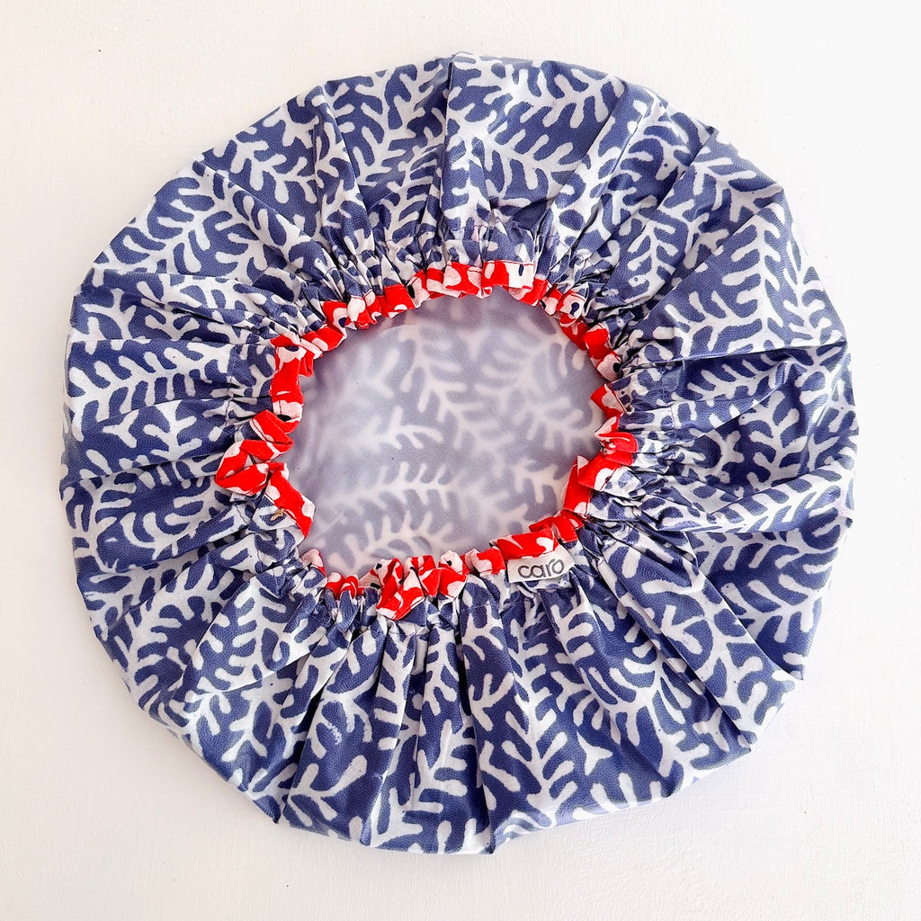 A round shower cap with a blue and white coral pattern, featuring a red elasticized inner trim and a white lining center panel, shown on a plain white background.