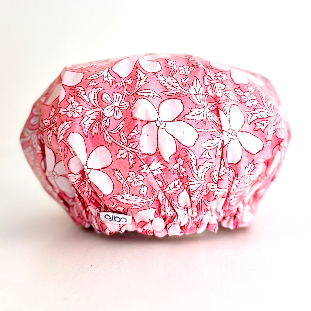A pink and white floral-patterned shower cap with elasticized edges, photographed on a clean white background. A small white brand tag reading 'caro' is visible near the bottom front.