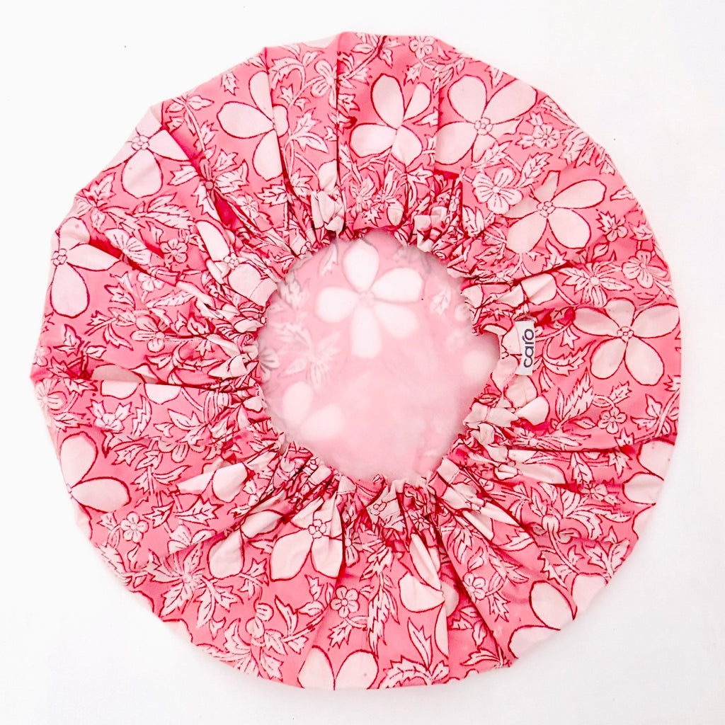 A pink and white floral-patterned shower cap with gathered elastic edges, shown on a plain white background with water dripping through the center.