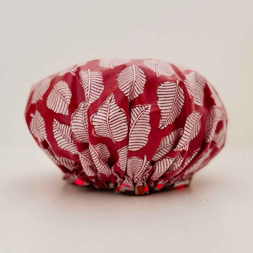 A red and white patterned cotton shower cap with a leaf print, photographed against a neutral light gray background.