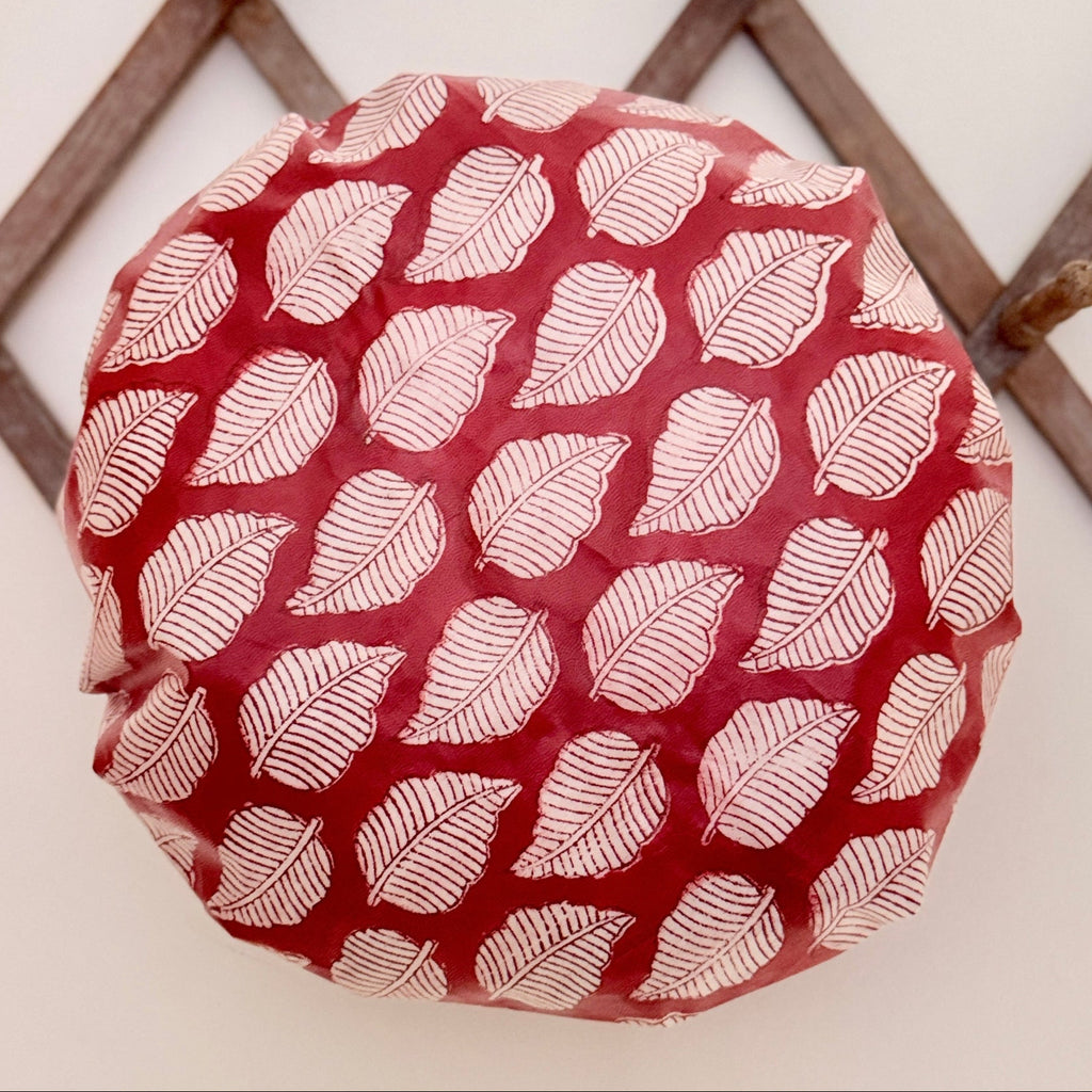 A Shower cap with a repeating white leaf pattern, photographed on a wooden lattice rack.