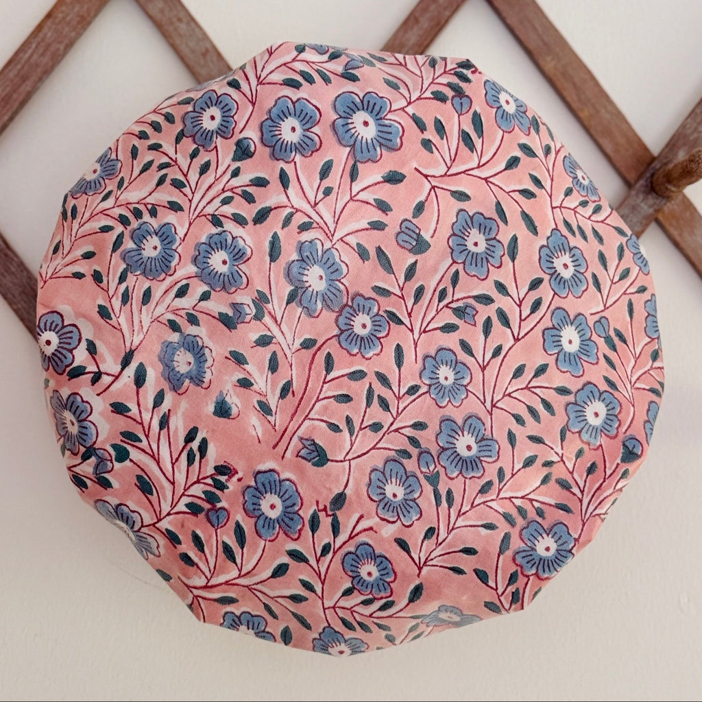 Shower Cap in pretty pink and blue floral pattern displayed on a light-colored surface with a wooden lattice 