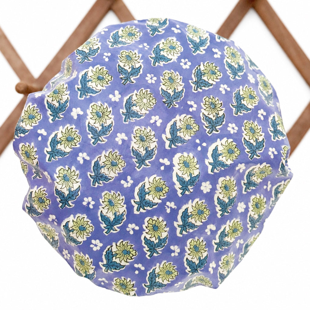 Blue, green and white floral print waterproof shower cap hanging on a  wooden lattice wall rack.