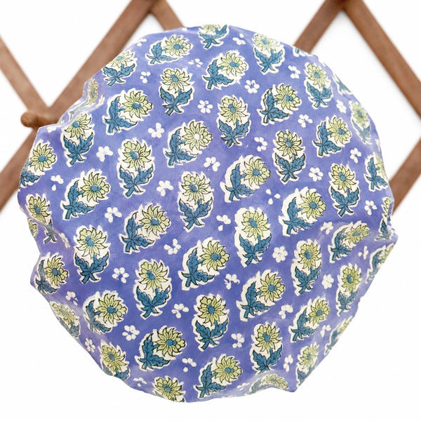 Blue, green and white floral print waterproof shower cap hanging on a  wooden lattice wall rack.