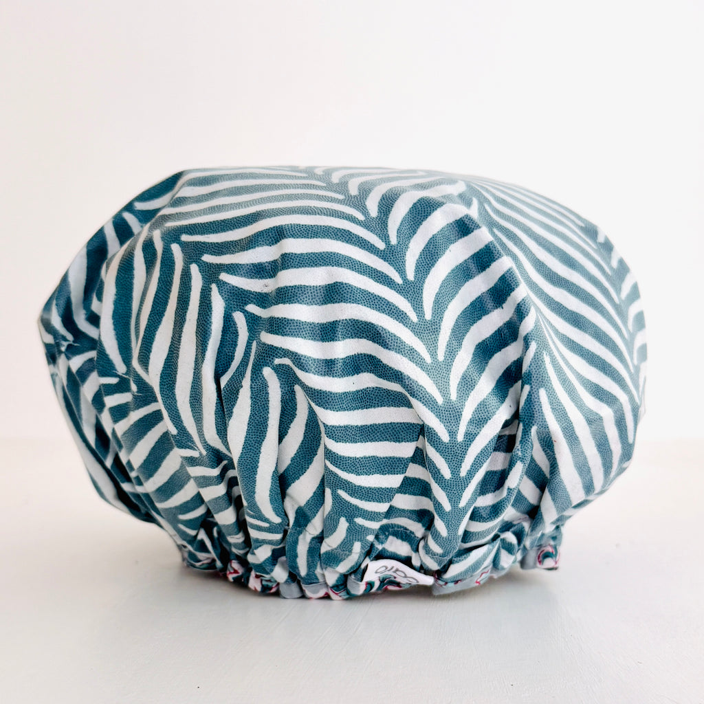 A shower cap with a teal and white palm leaf pattern, photographed against a plain white background.