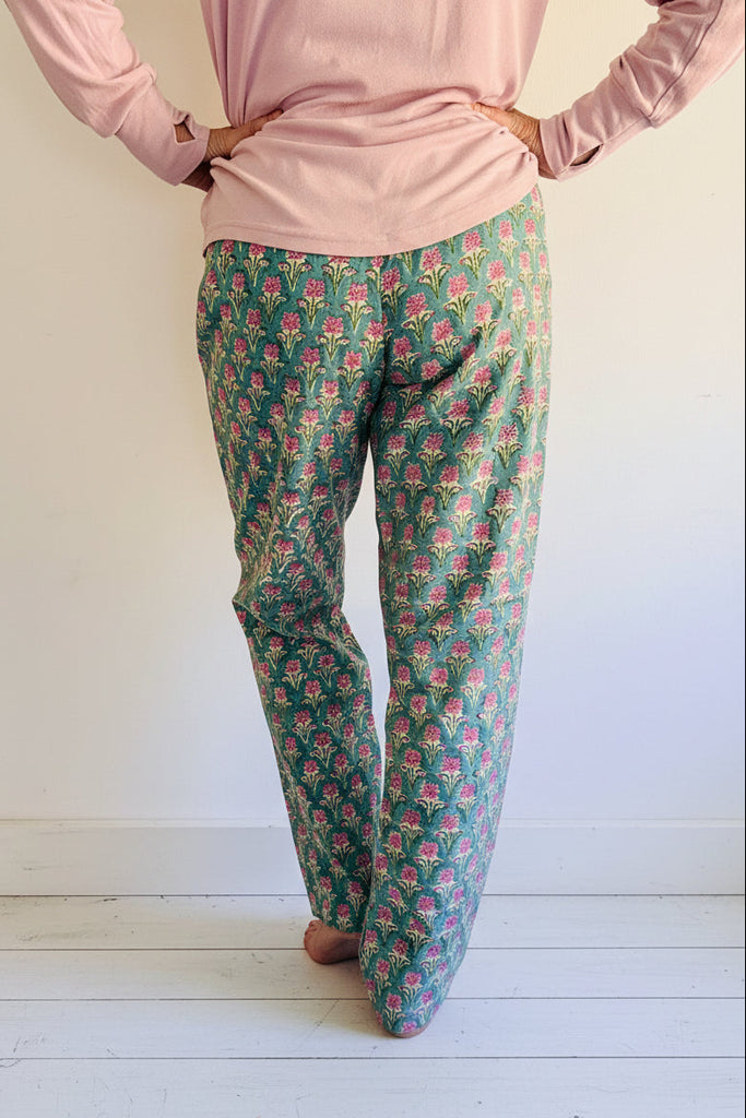 Person wearing pink long-sleeve top and green floral pants on a white background