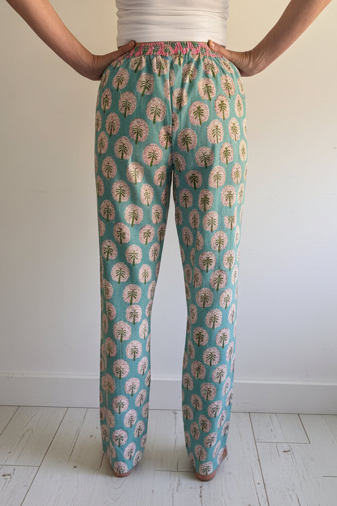 Back view of person wearing teal pants with floral pattern standing on white wooden floor.
