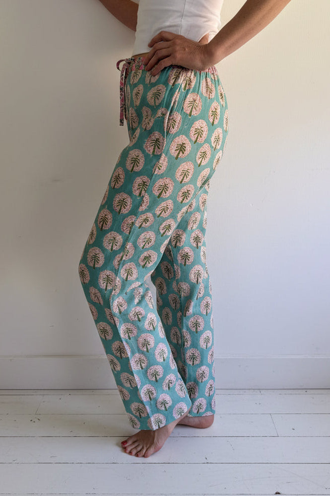 Person wearing a patterned teal and pink pants on a wooden platform against a white wall.