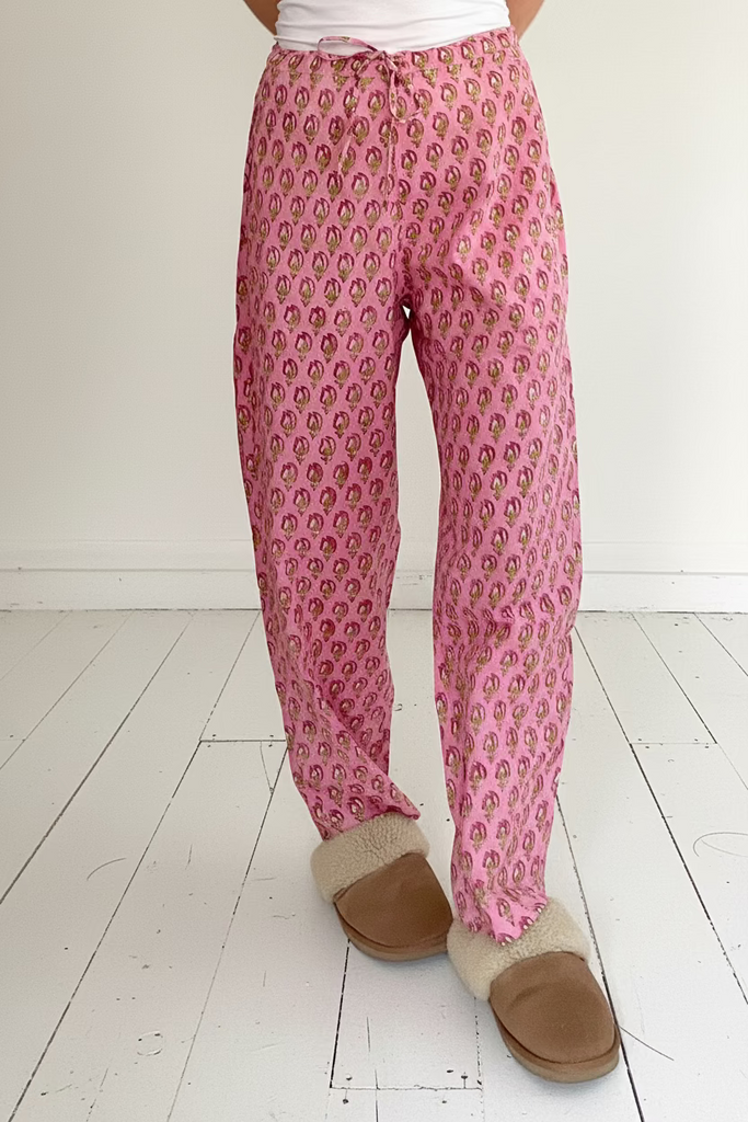 Woman's legs wearing pink floral print pyjama bottoms and sheepskin slippers on white background