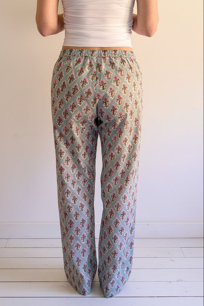 Person wearing floral patterned pants on a wooden pallet against a white wall