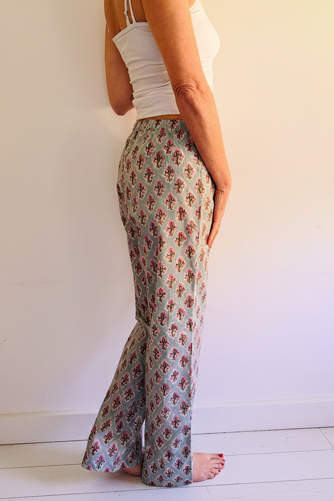 Person wearing floral patterned pants and a white top against a plain background