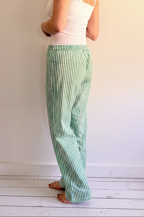 Woman wearing a white top and green striped pants standing against a white wall.