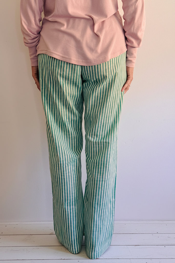 Person wearing green and white striped pants on a wooden floor against a plain background