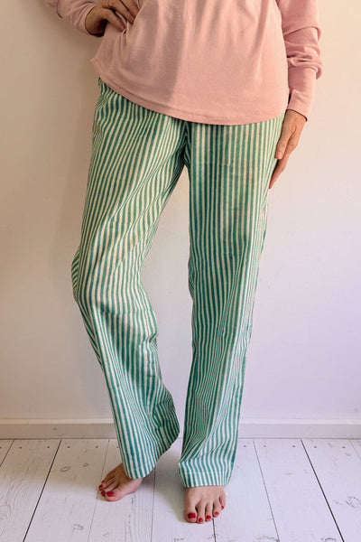Person wearing a pink top and green striped pants standing on white wooden floor