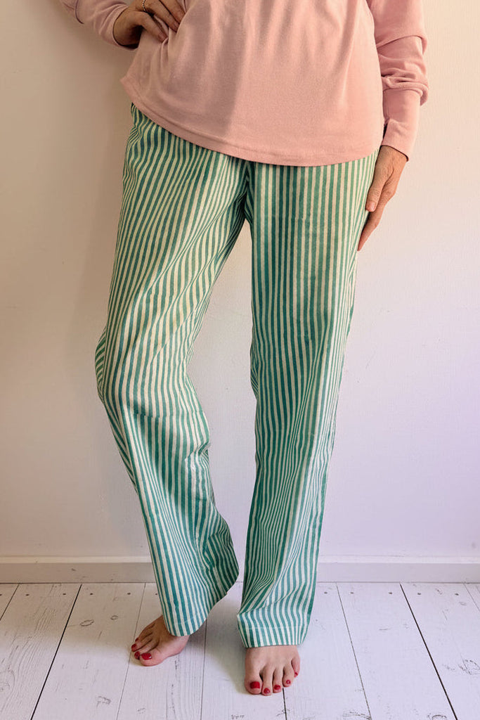 Person wearing a pink top and green striped pants standing on white wooden floor