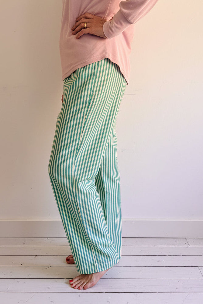 Person wearing a pink top and green striped pants standing on a wooden floor.