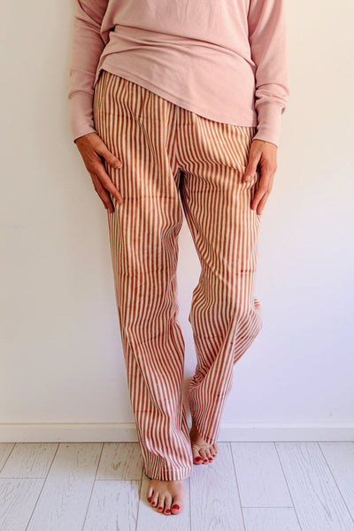 Person wearing a pink top and striped pants standing on wooden floor.