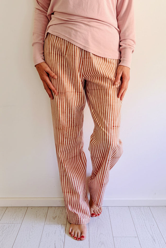 Person wearing a pink top and striped pants standing on wooden floor.