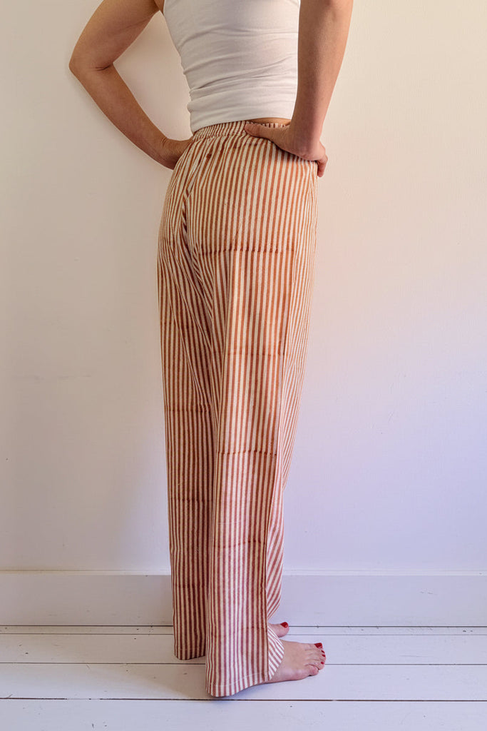 Person wearing striped pants and a white top on a white wooden floor.