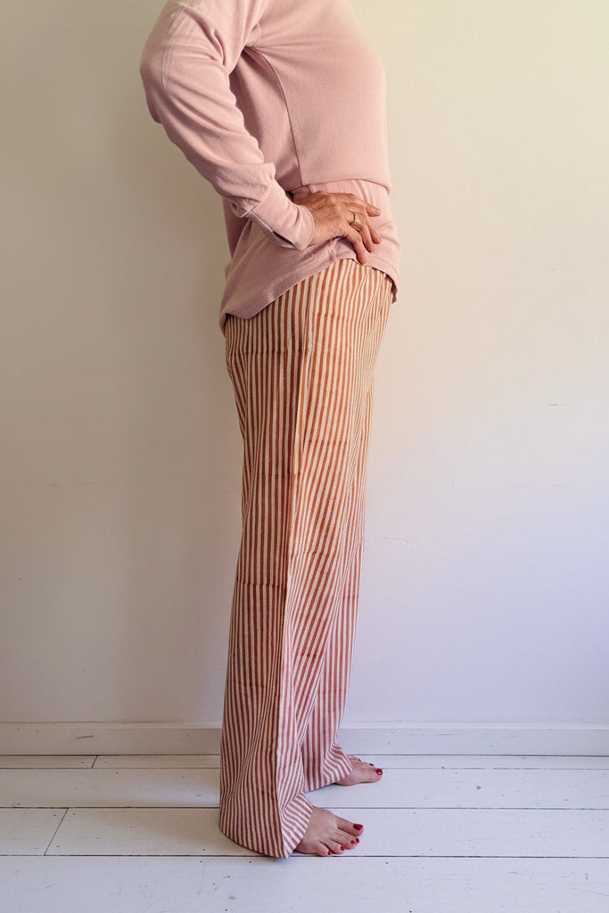 Person wearing a pink shirt and striped pants standing on a wooden floorboards