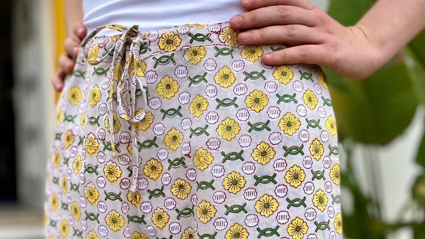 Person wearing a white top and floral-patterned pants with a blurred outdoor background