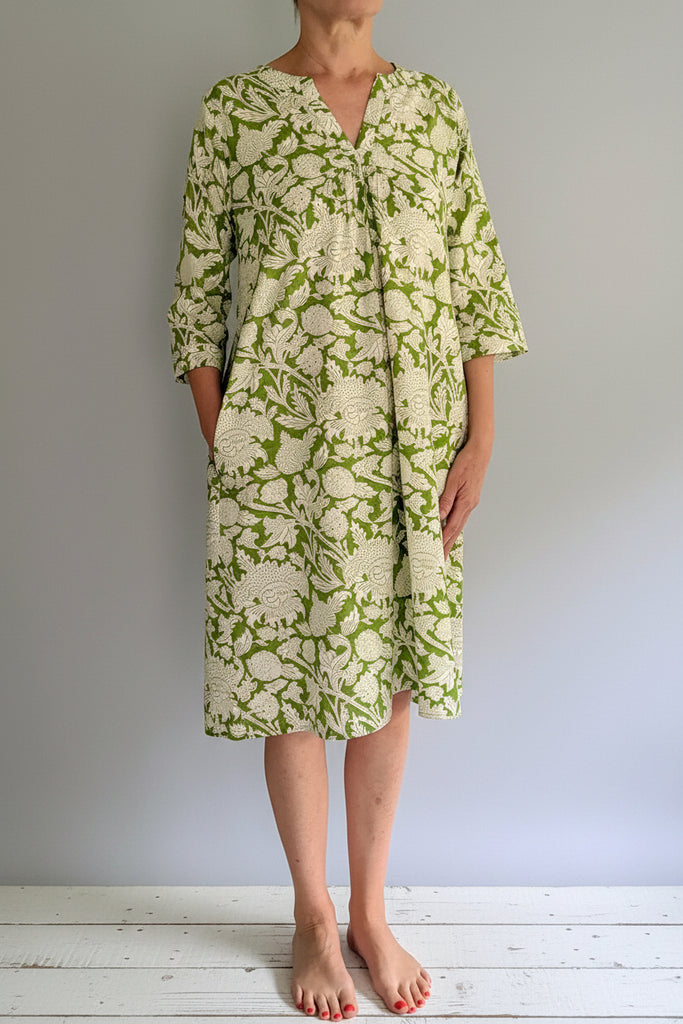 Person wearing a green and white patterned dress against a plain background