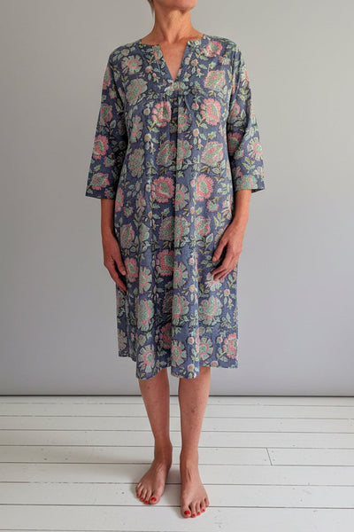 Woman wearing a floral dress standing against a white wall.