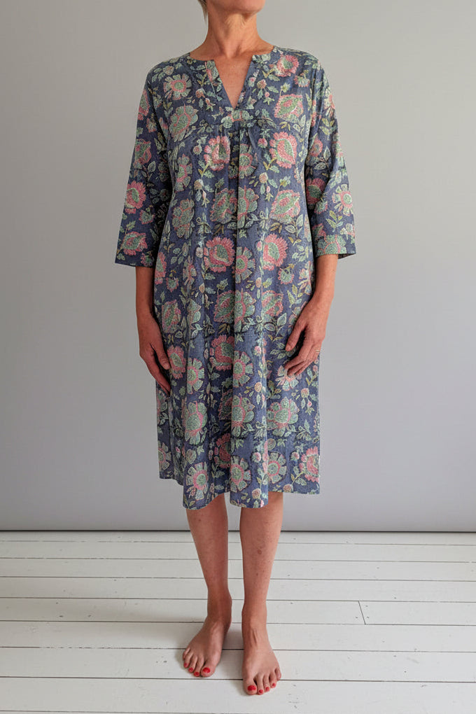 Woman wearing a floral dress standing against a white wall.