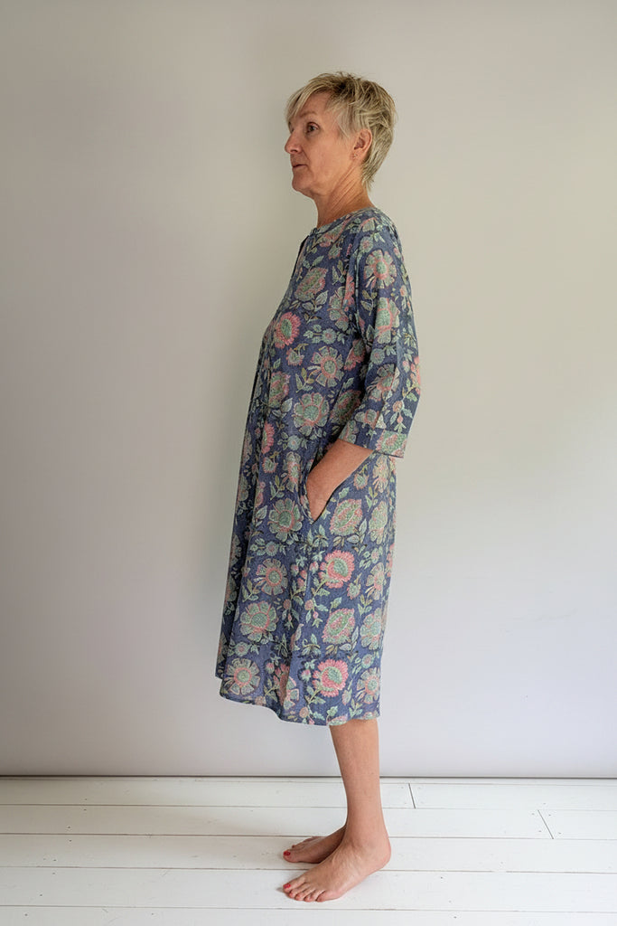 Woman wearing a floral dress standing against a plain background