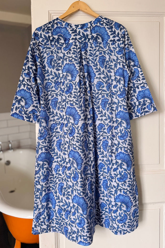 Blue floral kaftan nightdress hanging on a wooden hanger against a white door.