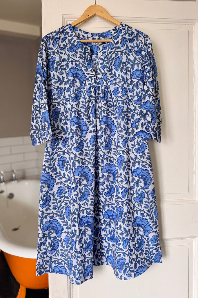 Blue floral nightdress hanging on a wooden hanger against a white door.