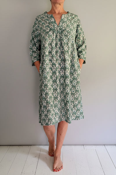 Woman wearing a green floral dress standing against a white background