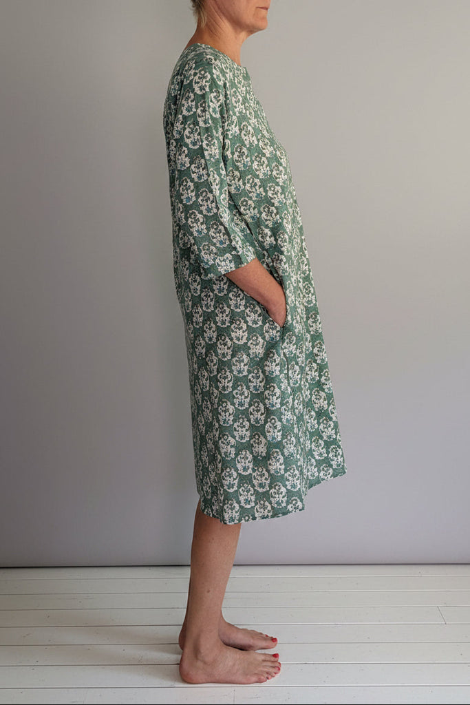 Person wearing a green floral dress standing against a white wall.