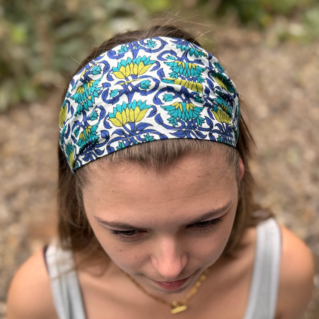 Person wearing a patterned headband sitting on a stone surface with greenery in the background